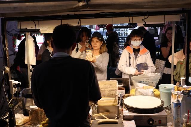 Tourists gather at a street food stall in Myeongdong Seoul as a vendor prepares a snack on a griddle Myeongdongs night market draws large crowds of foreign visitors seeking Korean street food AJP Yoo Na-hyun
