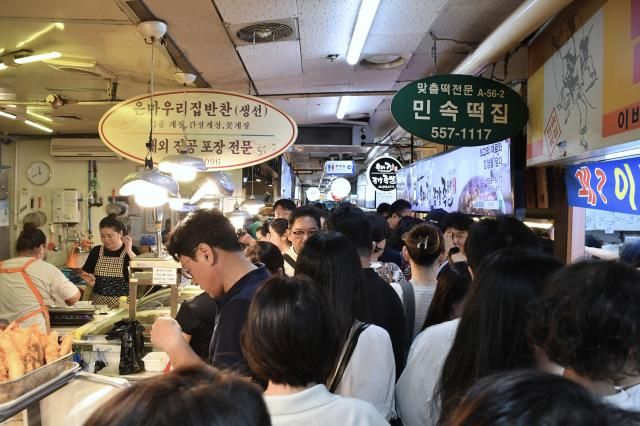 Shoulder to shoulder in the market corridor — shoppers packed between food stalls and small eateries under a maze of signs on Sept 25. AJP Joonha Yoo