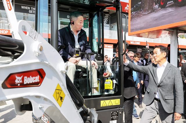 박정원 두산그룹 회장(왼쪽)이 바우마 2025에서 두산밥캣의 유럽시장 주력인 미니굴착기 신제품에 탑승해 스캇 박 두산밥캣 부회장(오른쪽)의 설명을 듣고 있다.