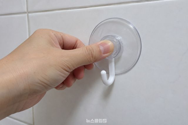 흰 욕실 타일에 붙인 투명 흡착 고리의 고무 테두리를 엄지로 누르는 모습. / 기사 이해를 돕기 위한 생성형 이미지