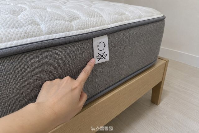 매트리스 옆면의 관리 표시 라벨을 손가락으로 가리켜 확인하고 있다. / 기사 이해를 돕기 위한 생성형 이미지