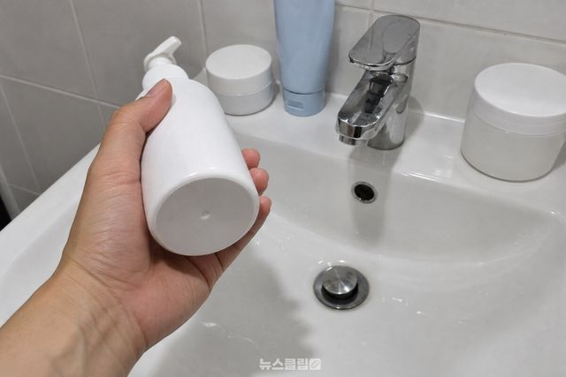 세면대 위에 꺼낸 화장품 통을 손으로 들어 바닥면을 확인하고 있다. / 기사 이해를 돕기 위한 생성형 이미지