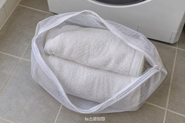세탁기 옆에 놓인 빨래망 속 수건이 서로 겹쳐 있는 모습 / 기사 이해를 돕기 위한 생성형 이미지