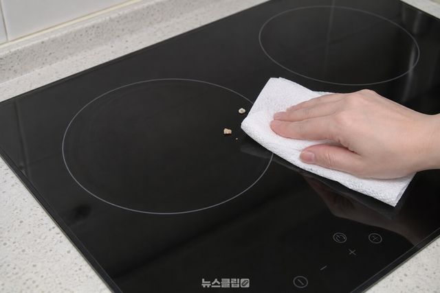 마른 키친타월로 식은 인덕션 상판의 굵은 음식물 조각을 한 방향으로 닦아내는 모습 / 기사 이해를 돕기 위한 생성형 이미지