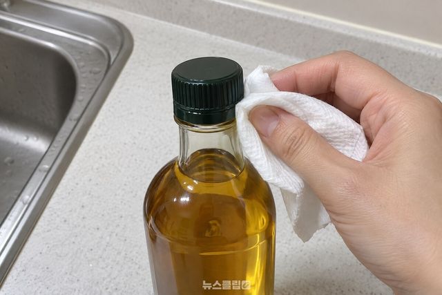 마른 휴지로 들기름 병목과 뚜껑 둘레를 닦고 있다. / 기사 이해를 돕기 위한 생성형 이미지