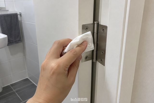 마른 휴지로 욕실 문 경첩의 겉면을 닦는 모습. / 기사 이해를 돕기 위한 생성형 이미지