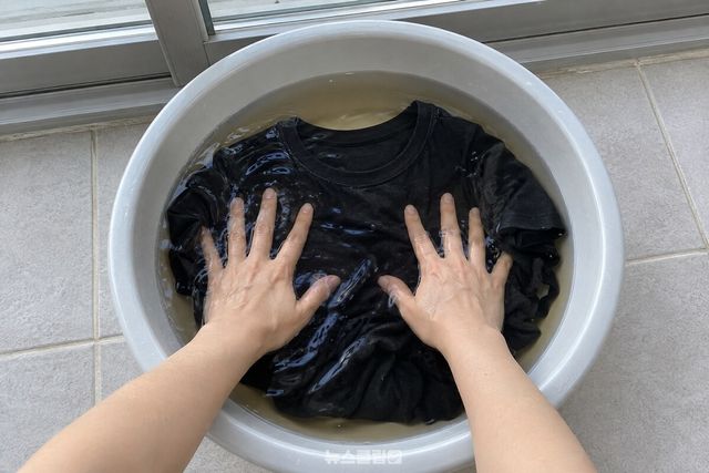 찬물과 맥주를 섞은 대야에서 검은 면 티셔츠를 손바닥으로 누르는 모습. / 기사 이해를 돕기 위한 생성형 이미지