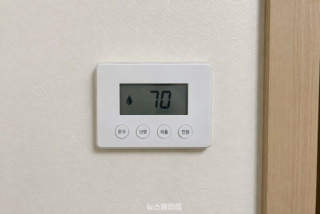 거실 벽에 붙은 보일러 온도조절기 화면에 온수 설정 숫자 70이 떠 있다. / 기사 이해를 돕기 위한 생성형 이미지