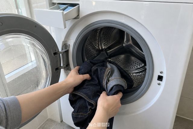 물기를 짠 청바지를 뒤집은 그대로 드럼세탁기 문 안으로 넣고 있다. / 기사 이해를 돕기 위한 생성형 이미지
