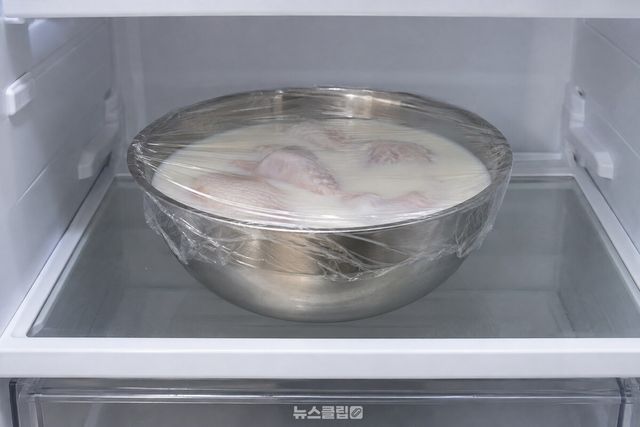 우유에 잠긴 생닭이 담긴 볼을 랩으로 덮어 냉장고 선반에 넣은 모습. / 기사 이해를 돕기 위한 생성형 이미지