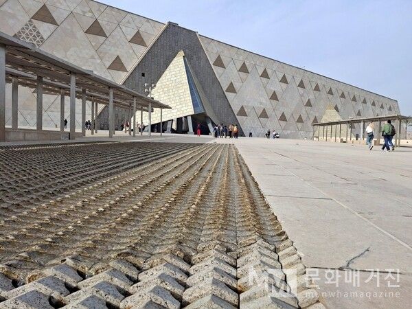 ▲ GEM의 삼각 패턴 외벽과 뒤집힌 삼각형 입구가 드러난 장면으로, 건물의 상징적인 디자인이 한눈에 보인다. 넓은 광장을 가로지르는 바닥 면은 사막과 피라미드의 질감을 현대적으로 표현하고 있다 / 사진: 한민광 제공