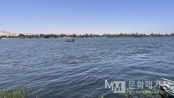 ▲ 이집트 Quna주 나일강. 나일강 위에 작은 배가 떠 있고, 강 너머로 야자수와 마을, 사막 산맥이 펼쳐져 있다 / 사진: 한민광 제공