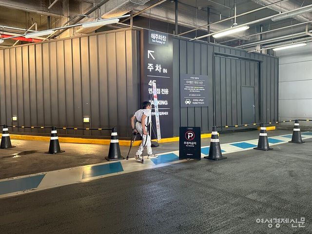 목발을 이용하는 이성수 씨가 용산 아이파크몰 장애인 전용 주차구역부터 출입구까지 보행 안전 통로를 통해 걸어가고 있다. 사진상 오른쪽은 차량이 들어오는 입구다. 보행 안전 통로와 차가 지나가는 경로가 겹칠 수밖에 없는 구조다. /여성경제신문