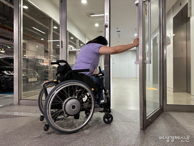 SK텔레콤 본사 지하 주차장과 연결되는 주 출입구 모습. 휠체어 이용자 홍서윤 씨(여·38)가 힘겹게 여닫이문을 열고 있다. /여성경제신문