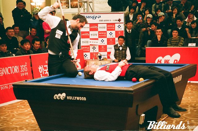 다니엘 산체스를 테이블 위에 뉘어 놓고 예술당구 시범을 보이는 세미 사이그너.