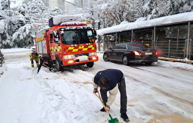 지난해 11월28일 오전 용인특례시 수지구 한 도로에서 소방차가 눈길에 발이 묶이자 소방관들이 염화칼슘 살포 및 긴급 제설 작업을 하고 있다. 경기일보DB