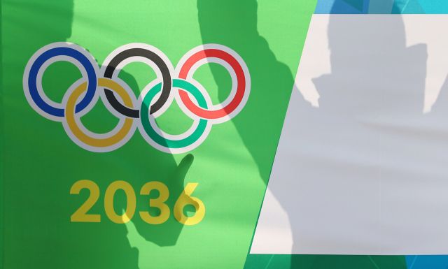 대한체육회 대의원총회를 통해 2036 하계 올림픽에 도전할 국내 유치 도시가 결정되는 28일 총회를 앞둔 서울 송파구 올림픽파크텔 앞에서 응원전을 펼치는 한 관계자의 모습이 오륜마크와 2036 숫자 위로 비치고 있다. 연합뉴스