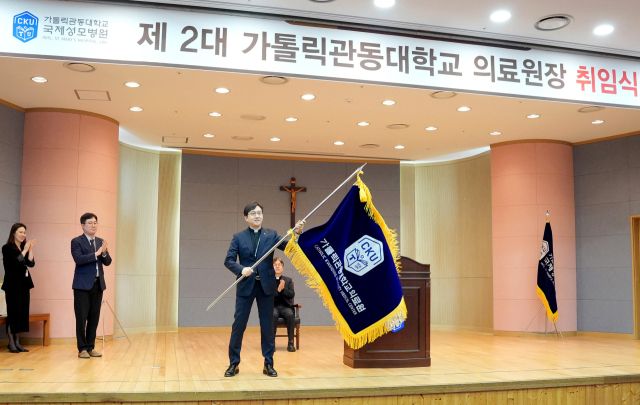 가톨릭관동대학교 국제성모병원 병원장인 고동현 신부가 제2대 가톨릭관동대학교 의료원장으로 취임, 의료원을 상징하는 의료원기를 들고 기념촬영을 하고 있다. 가톨릭관동대학교 국제성모병원 제공