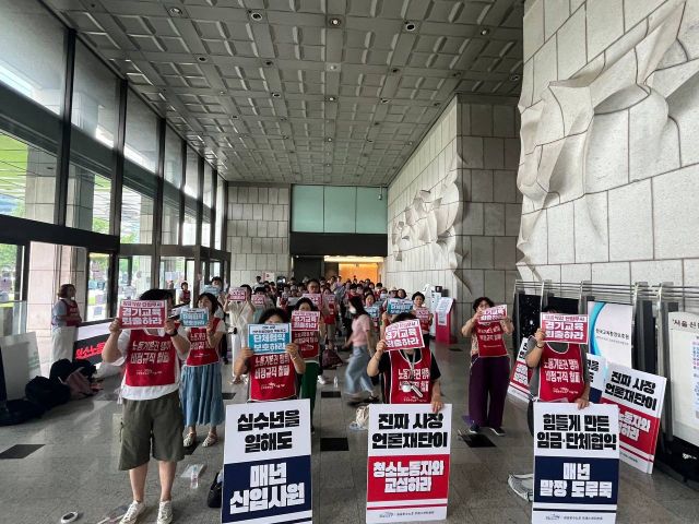 서울 중구 한국프레스센터 1층 로비에 청소노동자들이 붉은 조끼를 입고 ‘경기교육 퇴출하라’라고 적힌 피켓을 들고 서 있다. 공공운수노조 서울지부 제공