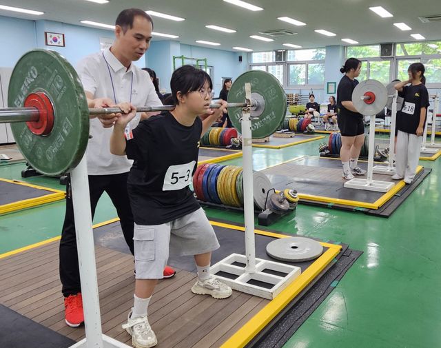 ‘2025 스포츠 영재 캠프’ 참가 여자 초등학생이 역도 종목을 체험하며 전문 지도자의 설명을 듣고 있다.경기체중고 제공
