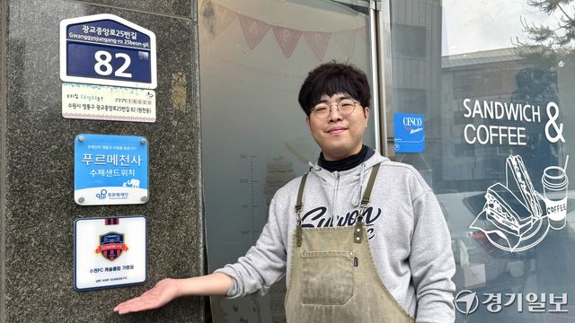 수원특례시 영통구 원천동에서 샌드위치 가게를 운영하는 구본빈씨(37)가 ‘수원FC 캐슬클럽 가맹점’ 현판을 소개하고 있다. 구씨의 가게는 수원FC ‘우리동네 캐슬클럽’ 제휴 매장으로 샌드위치 1개가 팔릴 때마다 100원씩 구단에 기부하고 있다. 김소현기자