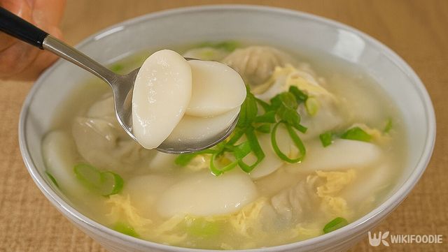 그릇에 담긴 떡만둣국을 숟가락으로 한술 뜨고 있다. / 위키푸디