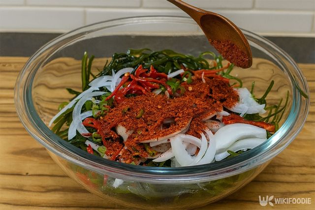 손질한 채소와 다시마채를 담은 볼에 고춧가루를 넣고 있다. / 위키푸디