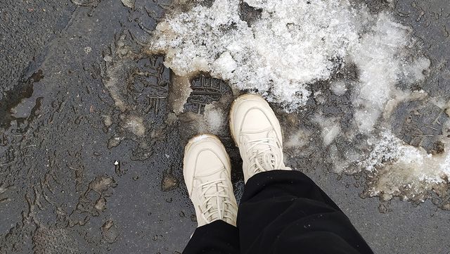 눈으로 덮인 아스팔트 위에 하얀 운동화를 신은 여자의 발이다. / Nataly_Video-shutterstock.com