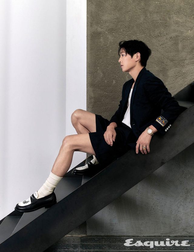 재킷, 티셔츠, 팬츠, 슈즈, 오토매틱 칼리버 LFT023을 탑재한 40mm 스틸 & 핑크 골드 케이스의 땅부르 워치, 화이트 골드 레 가스통 비통 라지 태그 펜던트 네크리스, 약지에 레이어링한 화이트 골드 앙프렝뜨 링과 옐로 골드 앙프렝뜨 링 모두 루이 비통.