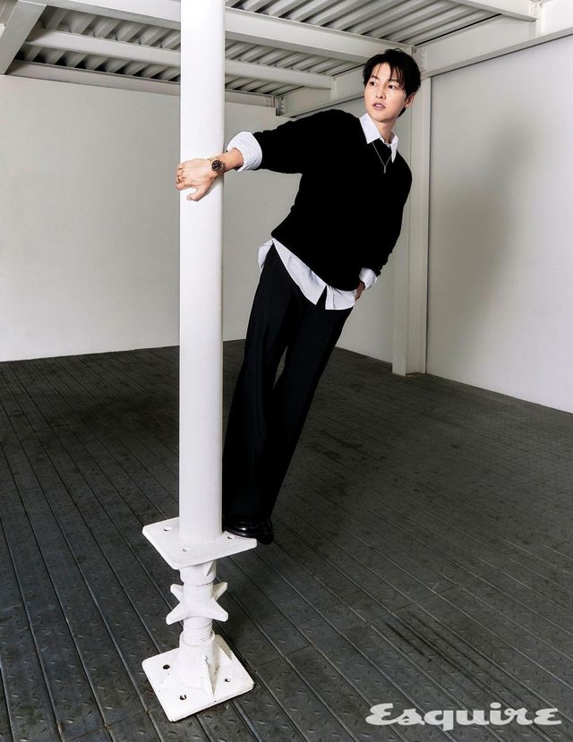 스웨터, 셔츠, 팬츠, 슈즈, 오토매틱 칼리버 LFT023을 탑재한 40mm 로즈 골드 케이스의 땅부르 워치, 옐로 골드 & 티타늄 소재의 레 가스통 비통 스몰 태그 펜던트 네크리스 모두 루이 비통.