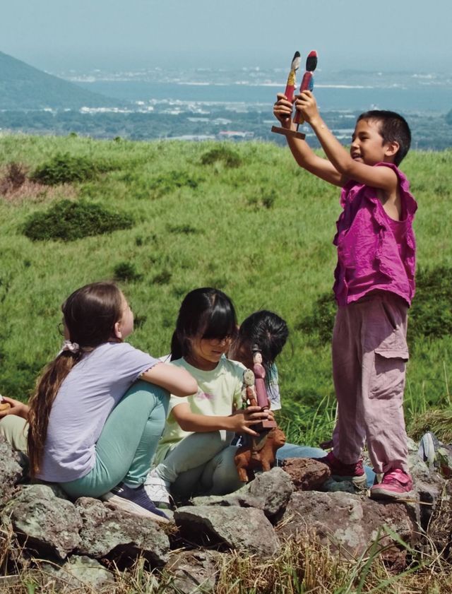 제인 진 카이센의 ‘Guardians’(2024)의 스틸 컷. 아이들이 무덤 주위를 뛰고, 꼭두를 들고 장난을 치며 웃는다. 