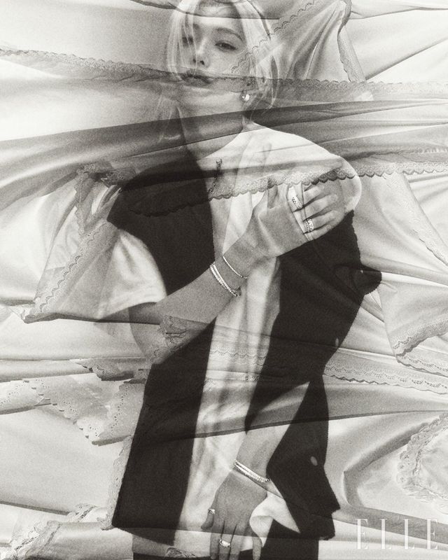 르 다미에 드 루이 비통 후프 이어링과 오른손 검지에 착용한 르 다미에 드 루이 비통 더블 링과 약지에 착용한 르 다미에 드 루이 비통 라지 링, 르 다미에 드 루이 비통 링, 레이어드한 르 다미에 드 루이 비통 브레이슬릿, 르 다미에 드 루이 비통 라지 브레이슬릿, 왼손에 착용한 두 개의 르 다미에 드 루이 비통 라지 브레이슬릿, 엄지와 중지에 착용한 르 다미에 드 루이 비통 라지 링, 쇼트 슬리브 카디건, 체인 디테일의 티셔츠, 블랙 팬츠는 모두 Louis Vuitton.