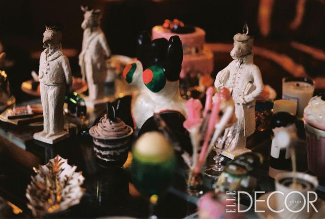  거실 테이블 중앙에는 니키 드 상팔의 조각 작품이 배치돼 있고, 그 주위에 마니시가 수집한 다양한 동물을 의인화한 조각상과 플라스틱 음식을 한데 모았다.