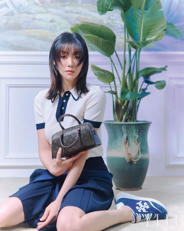 차주영이 착용한 비스코스 반팔 스웨터와 네이비 플리츠스커트, 허리에 두른 코튼 톱, 로고 디테일의 데스티니 트레이너 슈즈, 티 모노그램 코티드 캔버스 미니 배럴 백은 모두 Tory Burch.