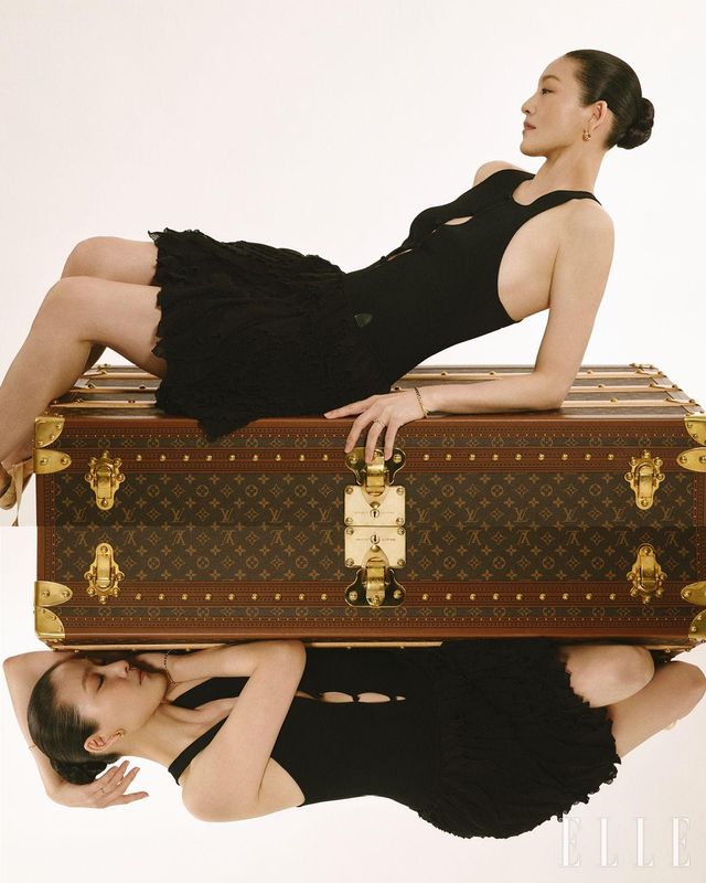 슬리브리스 프릴 드레스와 가죽 핸들이 달린 말 쿠리에 110 트렁크는 모두 Louis Vuitton. 옐로골드 소재의 르 다미에 드 루이 비통 이어링, 왼 손목에 착용한 옐로골드 소재의 미디엄 사이즈 르 다미에 루이 비통 브레이슬릿, 왼손 약지에 착용한 옐로골드 소재의 스몰 사이즈 르 다미에 루이 비통 링, 오른 손목에 착용한 옐로골드 소재의 스몰 사이즈 르 다미에 루이 비통 브레이슬릿은 모두 Louis Vuitton fine jewelry.