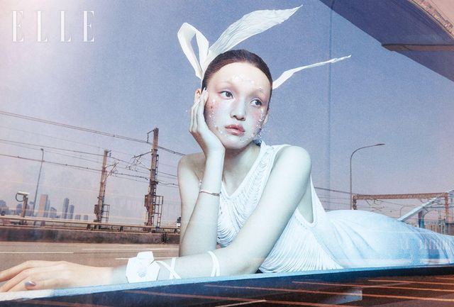 화이트 드레스는 Akris. 이어링은 Uselessobjects. 오른손의 브레이슬릿은 Swarovski. 왼손의 암 스트랩은 Ice Dust. 날개는 Kowgi.