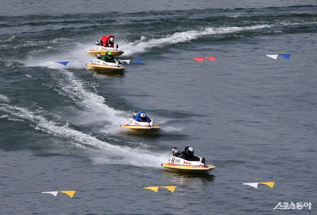 미사경정장에 등바람이 부는 가운데, 선수들이 결승선을 향해 질주하고 있다.