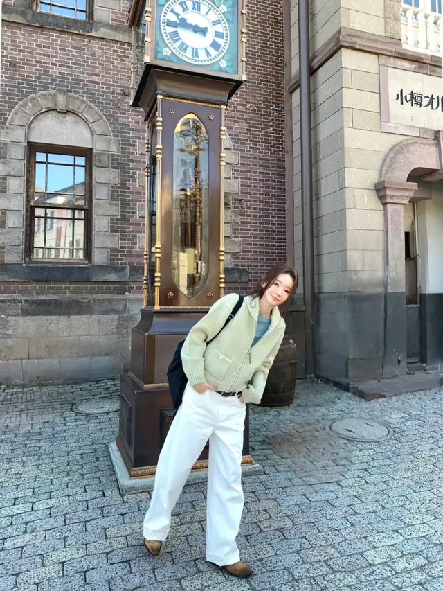 강민경이 고풍스러운 시계탑 앞에서 산뜻한 파스텔 니트 집업으로 완성한 겨울 라이트룩을 선보이며 포즈를 취하고 있다. /사진=강민경 인스타그램