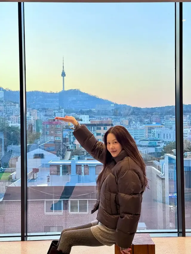 유리창 너머로 보이는 남산 풍경을 배경으로 고현정이 브라운 패딩룩의 서정적인 무드를 연출한다. /사진=고현정 인스타그램